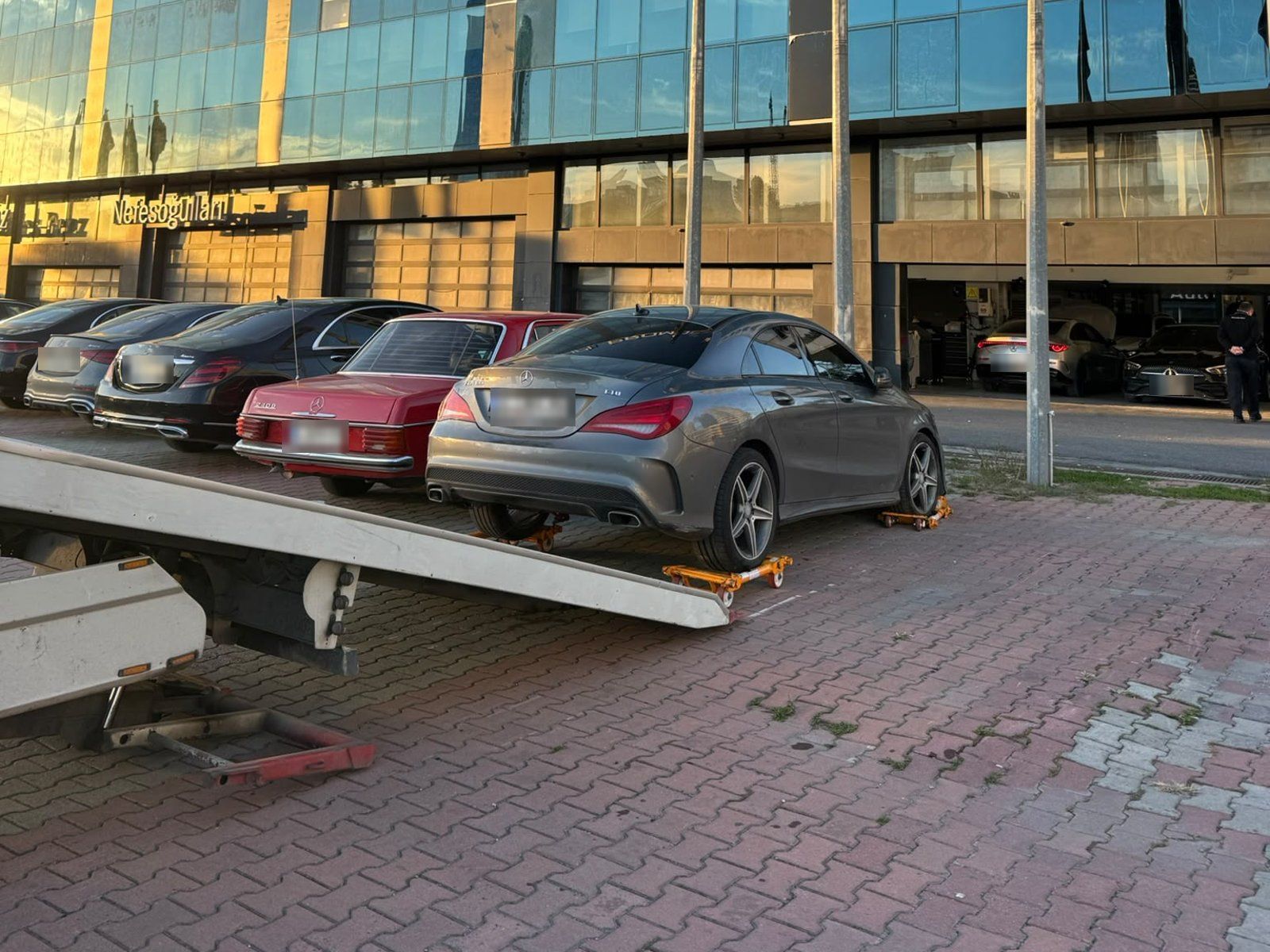 Tekerlekleri altında sarı taşıma aparatları olan otomobil, arkada rampası indirilmiş kayar kasalı çekici